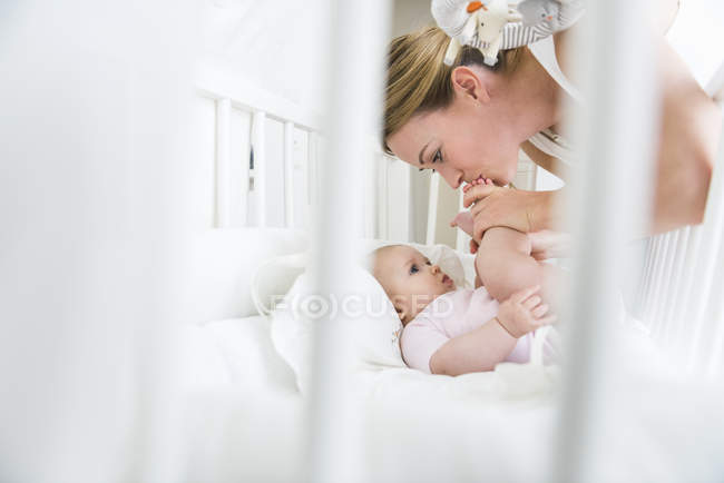 Мать целует детские ножки в кроватке — стоковое фото