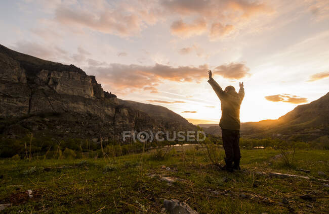 Homem em pé no cenário rural, braços erguidos em direção ao sol — Fotografia de Stock