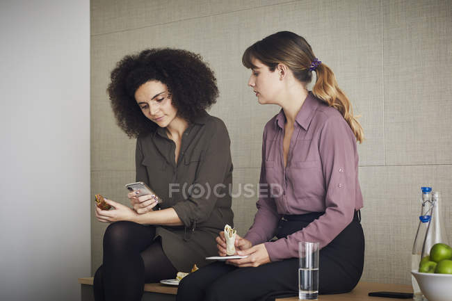 Colleagues having lunch and looking at smartphone — Stock Photo