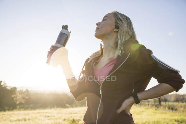 Jovem segurando garrafa de água e se exercitando ao ar livre — Fotografia de Stock