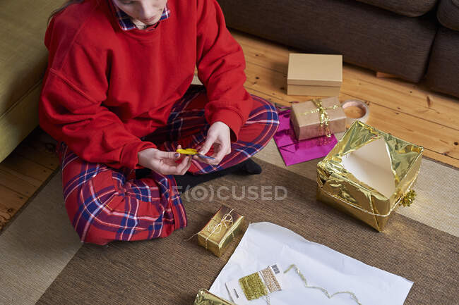 Mujer joven sentada en el piso de la sala de estar envolviendo regalos, vista aérea recortada - foto de stock
