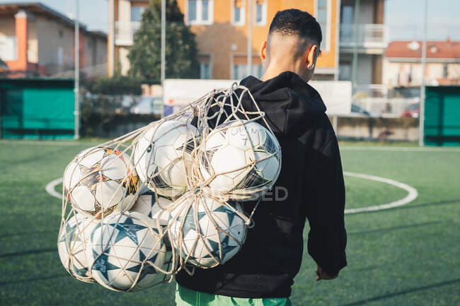 Football player carrying net of balls on pitch — Stock Photo