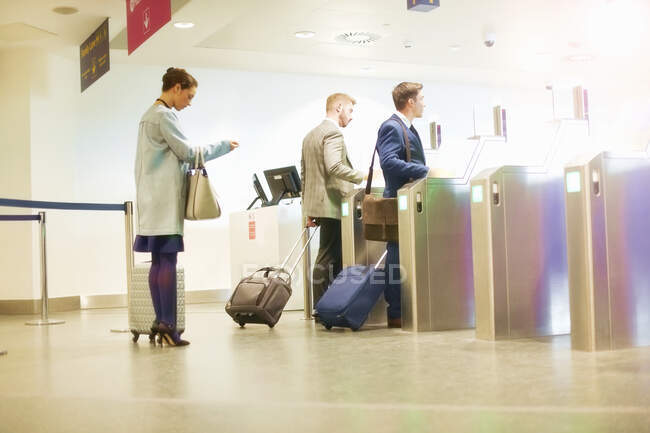 Бизнесмены и женщины, проходящие через ворота безопасности в аэропорту, вид сбоку — стоковое фото