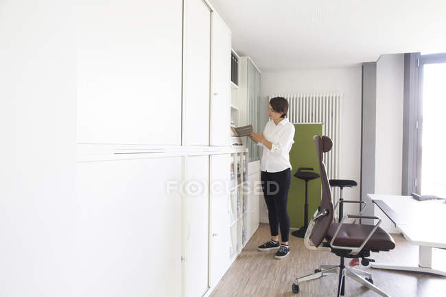 Young female sale manager looking at sales brochure in office furniture store — Stock Photo
