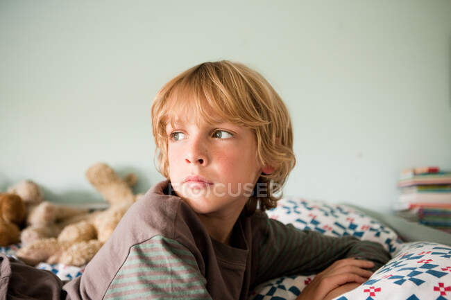 Jeune garçon couché sur le lit regardant au loin — Photo de stock