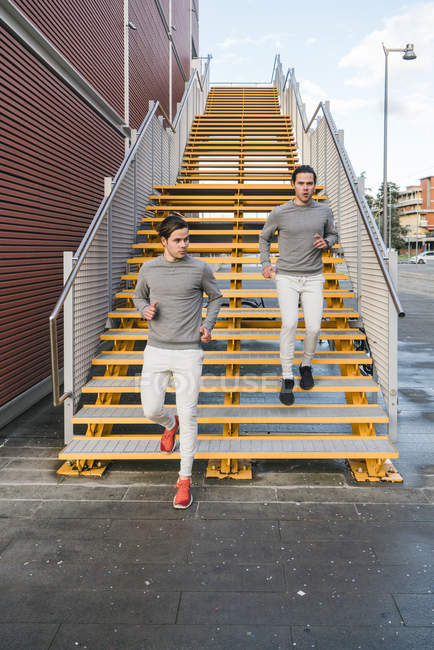 Young male twins running down on city stairway — Stock Photo