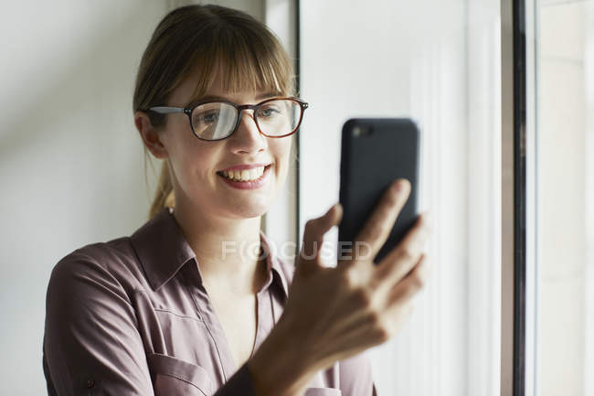 Woman in eyeglasses looking at smartphone and smiling — Stock Photo
