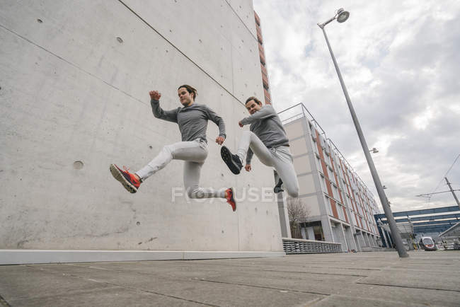 Young male twin running and jumping mid air on city sidewalk — Stock Photo