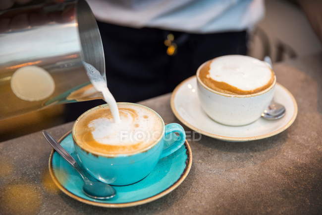 Barista pouring frothy milk into coffee cup, close-up — Stock Photo