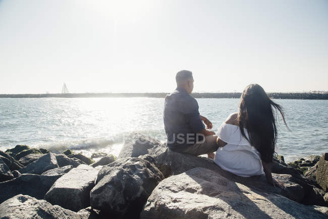 Casal sentado em rochas costeiras, olhando para a vista, visão traseira — Fotografia de Stock