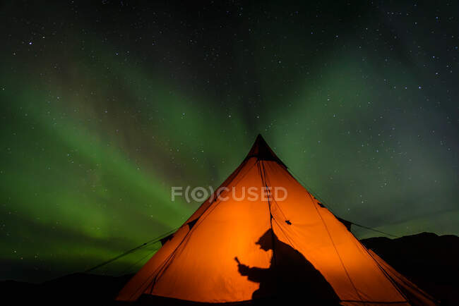 Camper reading inside tent, Aurora Borealis in background, Narsaq, Vestgronland, Groenlândia — Fotografia de Stock