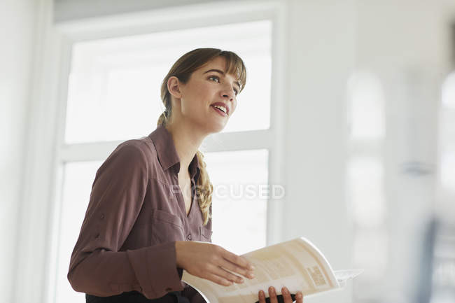 Businesswoman in office holding paperwork and smiling away — Stock Photo