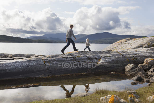 Man and son walking on fjord rock formation, Aure, More og Romsdal, Noruega - foto de stock