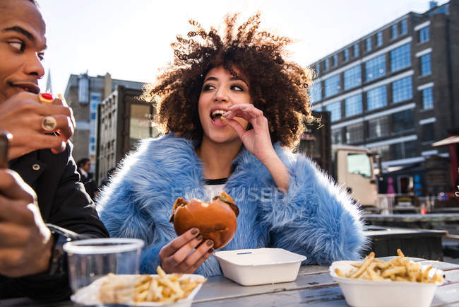 Pareja joven comiendo hamburguesa y papas fritas al aire libre - foto de stock