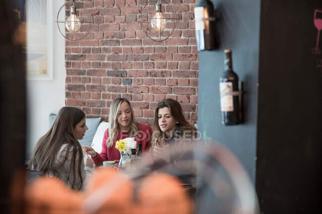 Female friends sitting together in cafe, looking at smartphone — Stock Photo