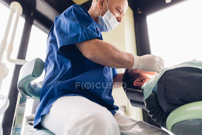 Dentiste effectuant une procédure dentaire sur le patient masculin — Photo de stock