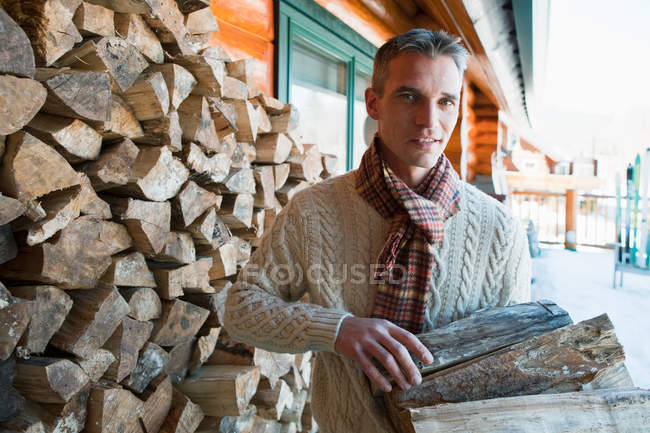 Retrato del hombre sosteniendo troncos cerca de casa - foto de stock