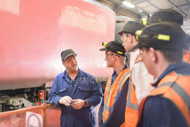 Engineer instructing apprentices with locomotive wheel lathe in train engineering factory — Stock Photo