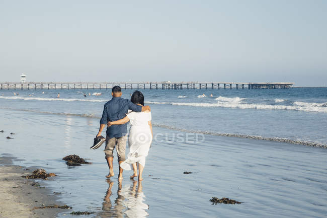 Couple walking along beach, barefoot, rear view — Stock Photo