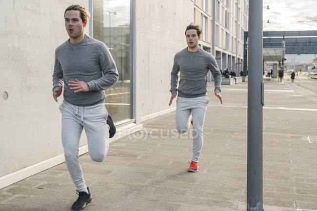 Young male twin running along city sidewalk — Stock Photo