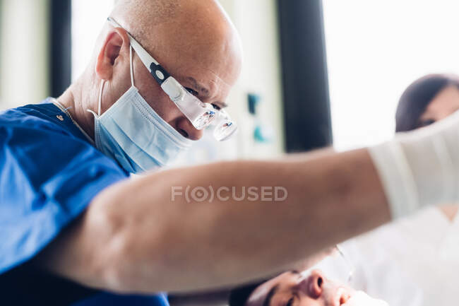 Dentista que realiza procedimiento dental en paciente masculino - foto de stock