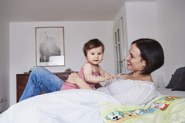 Mother and baby daughter relaxing on bed — Stock Photo