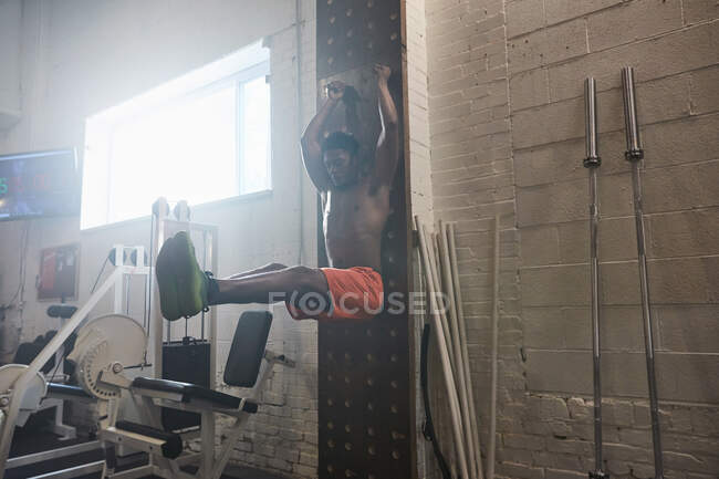 Man in gym using exercise equipment, doing leg pull ups — Stock Photo