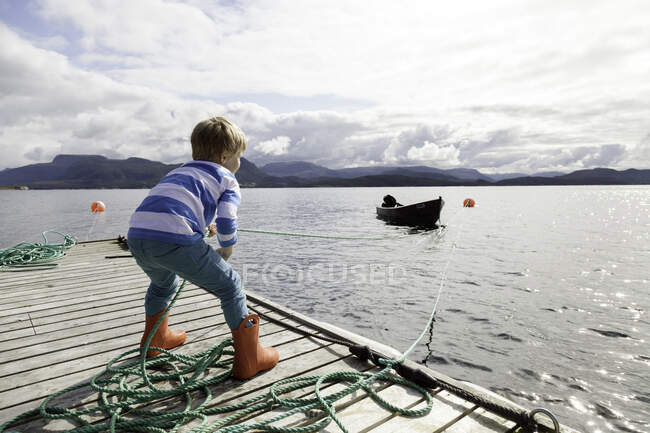 Chico en muelle tirando de barco fiordo por cuerda, Aure, Más og Romsdal, Noruega - foto de stock