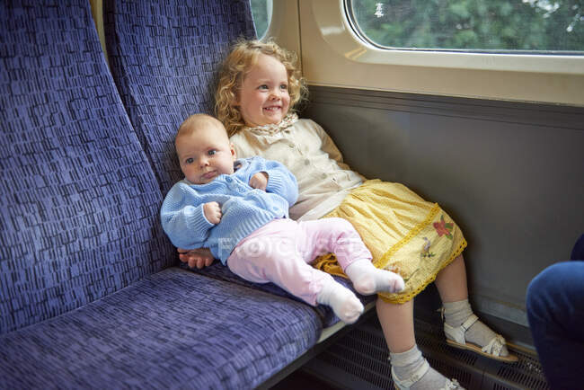 Female toddler sitting on train with baby sister — Stock Photo