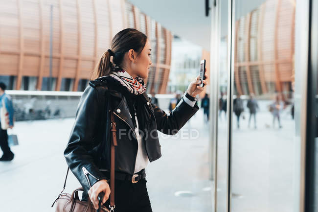 Mujer usando smartphone y llevando equipaje - foto de stock