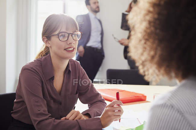 Mujer de negocios en el escritorio de la oficina hablando con su colega - foto de stock