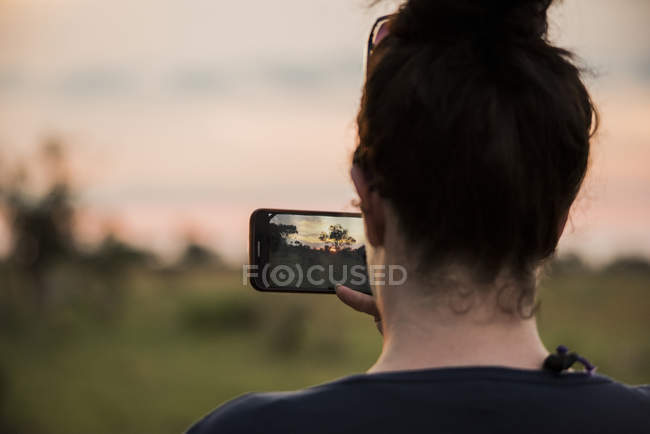 Vue arrière de Jeune femme photographiant avec smartphone sur Okavango Delta, Botswana, Afrique — Photo de stock