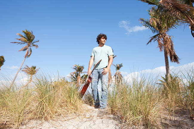 Молодий чоловік тримає гітару на пляжі — стокове фото