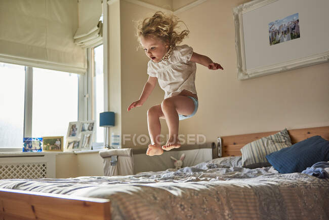 Kleinkind springt mitten in der Luft auf Bett — Stockfoto