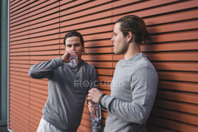 Jovens gêmeos do sexo masculino fazendo pausa de treinamento e bebendo água engarrafada — Fotografia de Stock