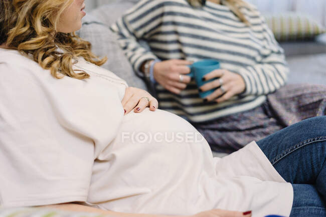 Mujer embarazada y amigo en el sofá, recortado - foto de stock