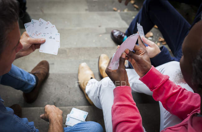 Tre uomini maturi seduti su gradini con carte da gioco — Foto stock