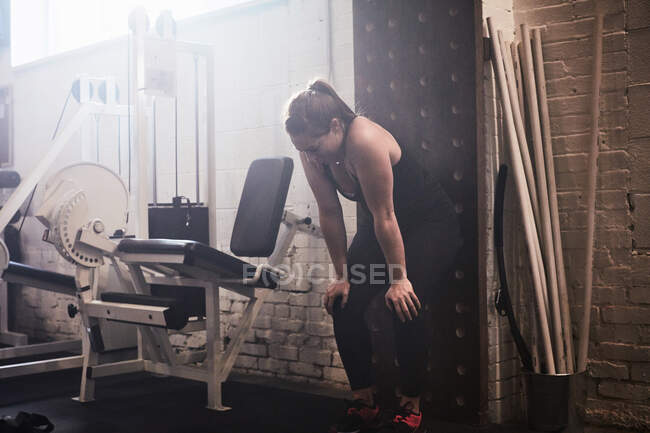 Woman in gym, hands on knees exhausted — Stock Photo