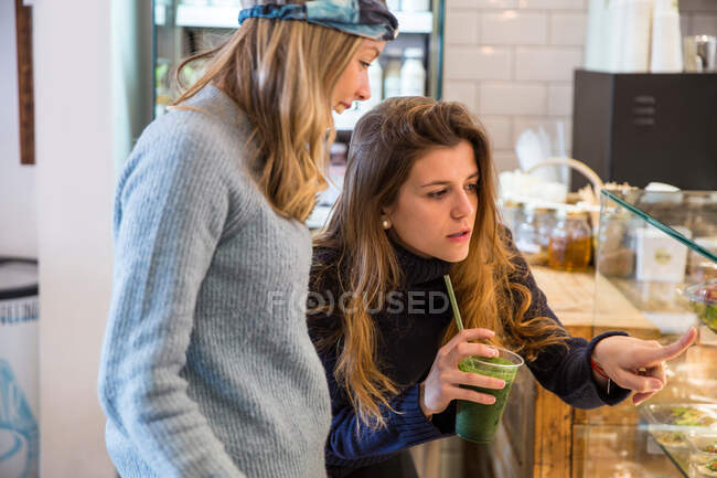 Giovane donna e amico guardando vetrina cibo fresco in caffè — Foto stock