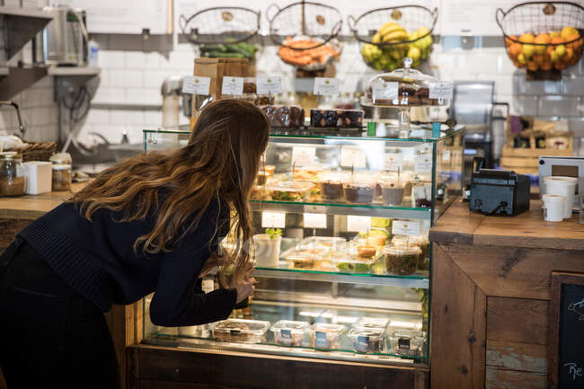 Jovem mulher olhando para o armário de exibição de alimentos frescos no café — Fotografia de Stock