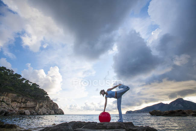 Frau mit Medizinball auf Felsen stehend, Palma de mallorca, islas baleares, spanien, europa — Stockfoto