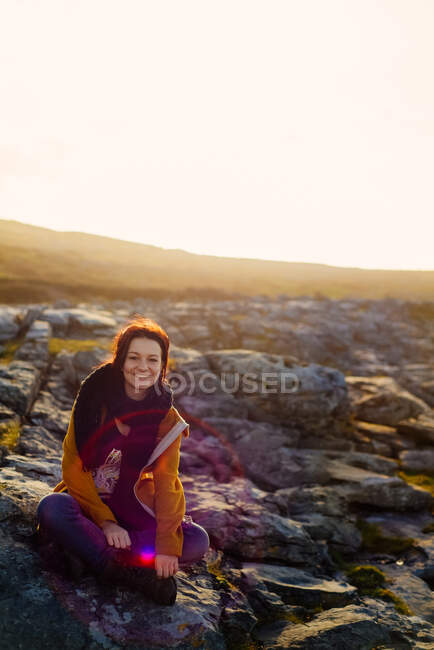 Mujer sentada en las rocas, Fanore, Clare, Irlanda - foto de stock