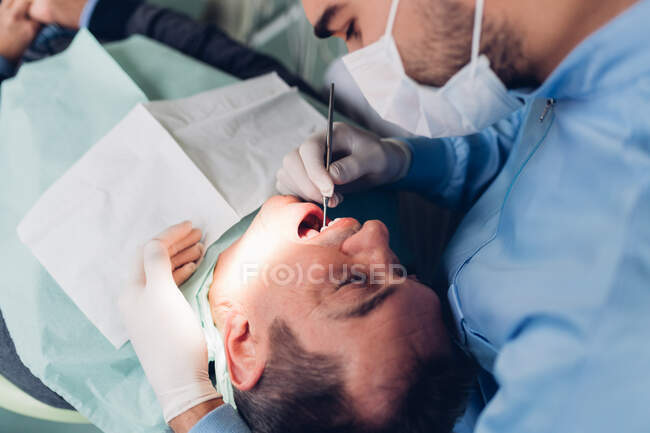 Dentiste regardant dans la bouche du patient masculin, vue surélevée — Photo de stock