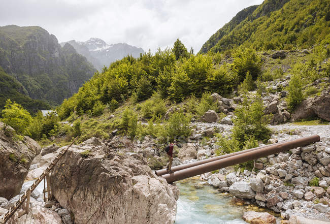 Homme traversant la rivière sur des tuyaux pont, montagnes maudit, Theth, Shkoder, Albanie, Europe — Photo de stock