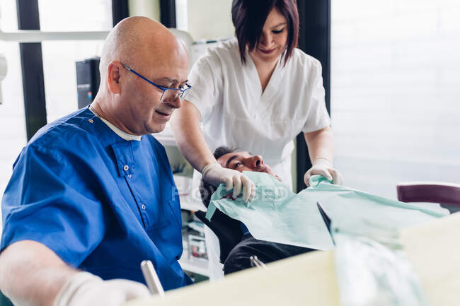 Стоматолог и зубная медсестра готовят пациента мужского пола к лечению — стоковое фото