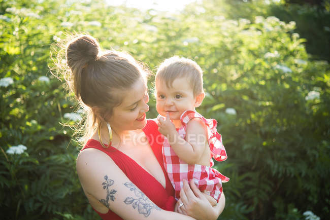 Woman carrying baby girl in arms in garden — Stock Photo