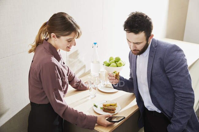 Uomo e donna d'affari che guardano lo smartphone durante il pranzo di lavoro — Foto stock