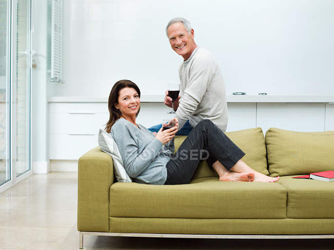 Pareja madura sentada en sofá con vino - foto de stock
