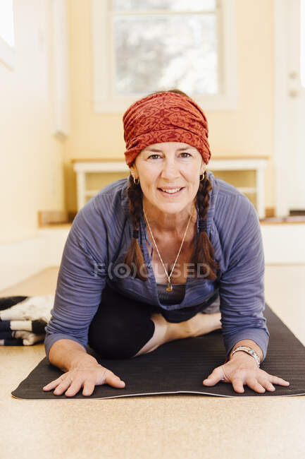 Retrato de mujer mayor practicando pájaro yoga pose (kapotasana) en estudio de yoga - foto de stock