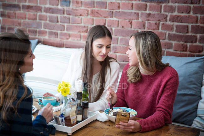 Tres amigas sentadas juntas en la cafetería - foto de stock